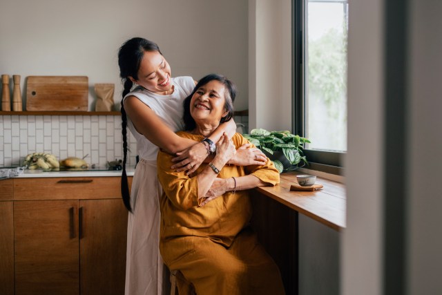 A smiling woman enjoying drinking tea while her loving daughter is embracing her.